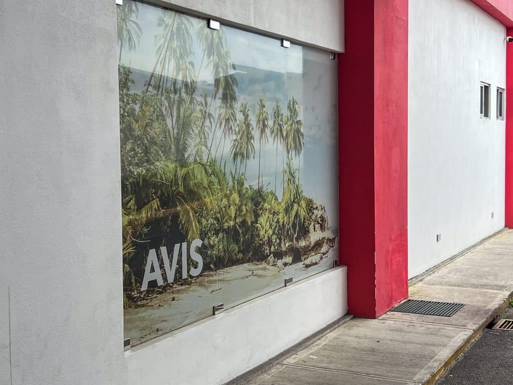 White painted side wall of the AVIS car hire centre in San Jose, Costa Rica. Decorated with tropical beach photograph and red painted columns