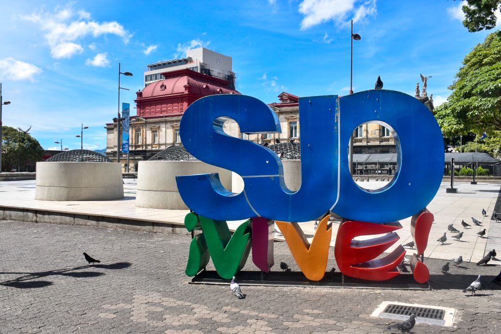 Colourful letter sign saying Vive SJO in square to the side of the National Theatre building, San Jose, Costa Rica