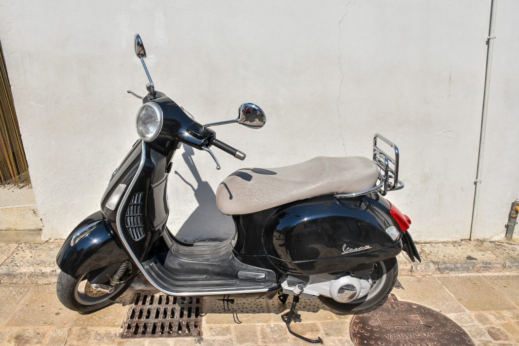 Black moped with white leather seat parked on a stone floor in front of a white wall
