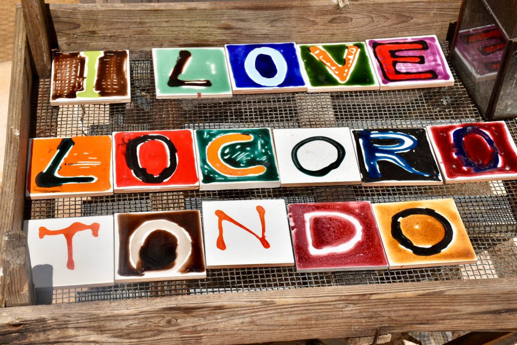 Display of square ceramic tiles of many colours each with a letter on, spelling I Love Locorotondo (which is a town in Puglia)