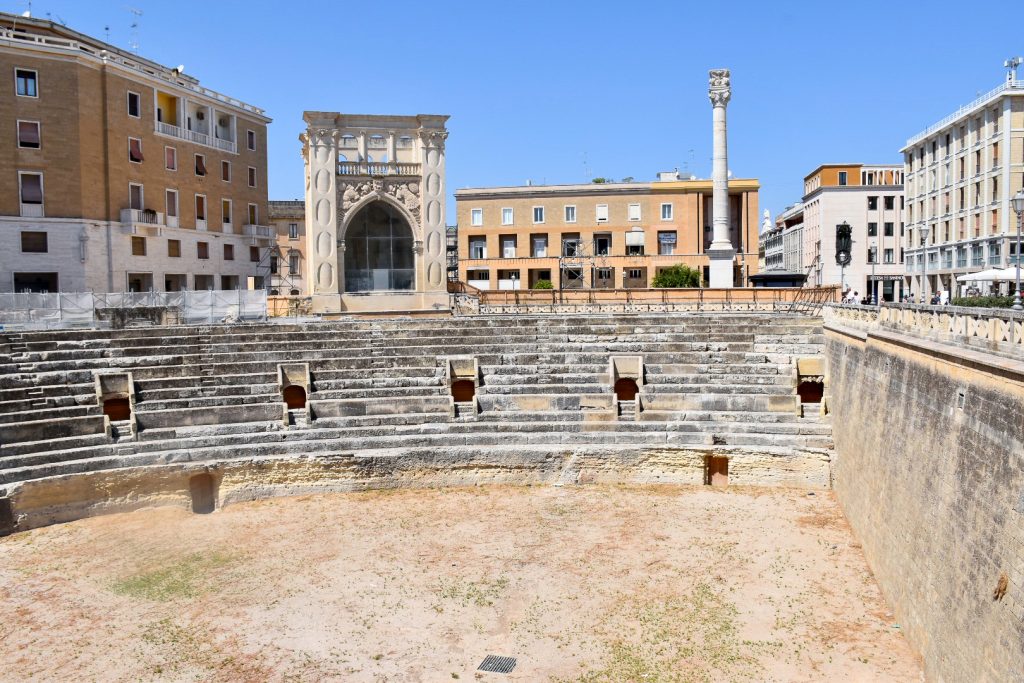 Section of roman amphitheatre seating (one tier) with town buildings and a column set behind the seating