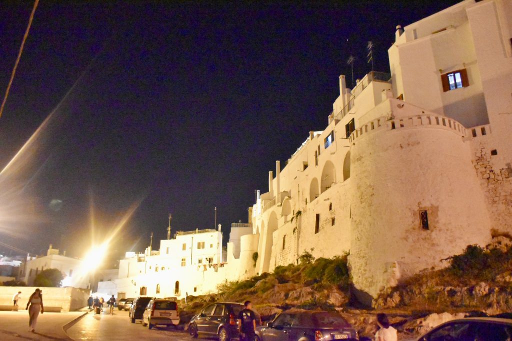 Black night sky. White fortified walls illuminated by electric lights