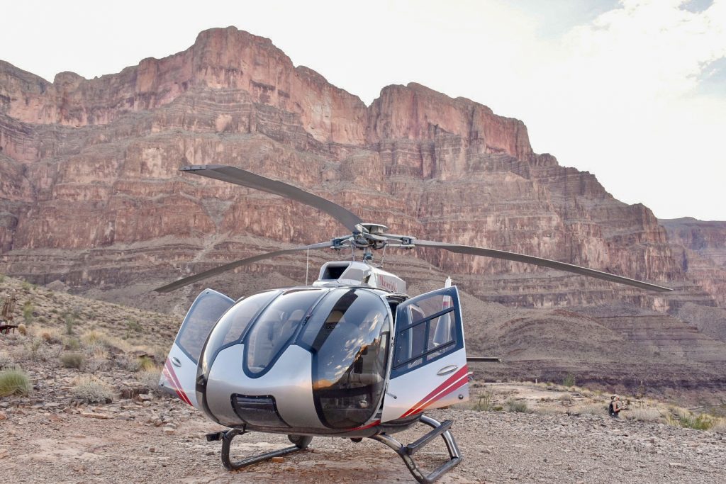 Silver and black helicopter in front of photo with jagged rocks of canyon behind