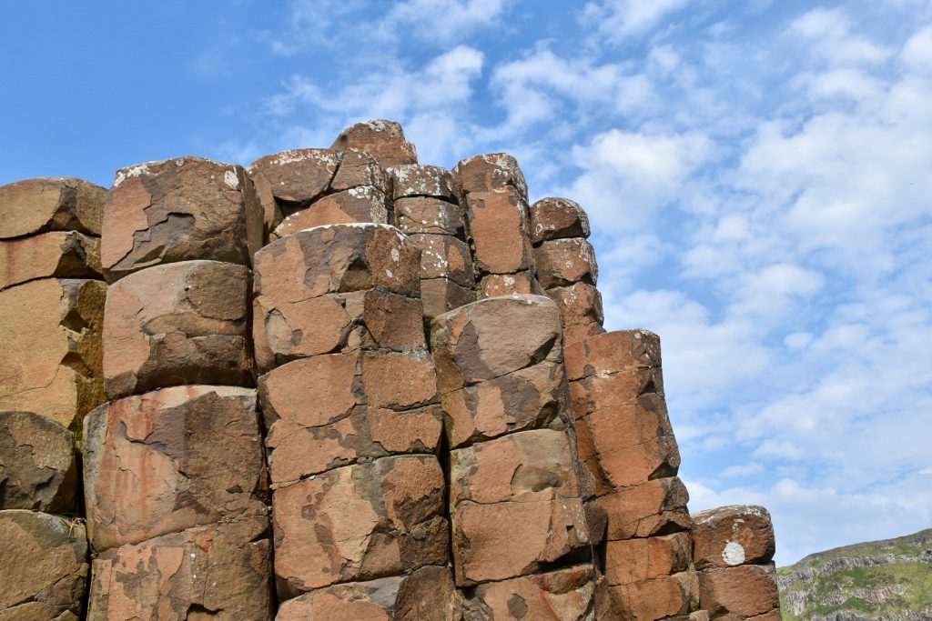 Orange/Brown rock formation in left hand side of picture - rocks appear as columns closely packed together. Blue sky and some light white clouds behind