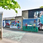 Concrete buildings with political murals across a road with an open gate on the left hand side