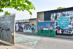 Concrete buildings with political murals across a road with an open gate on the left hand side