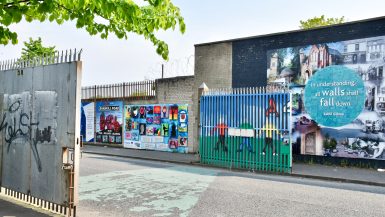 Concrete buildings with political murals across a road with an open gate on the left hand side