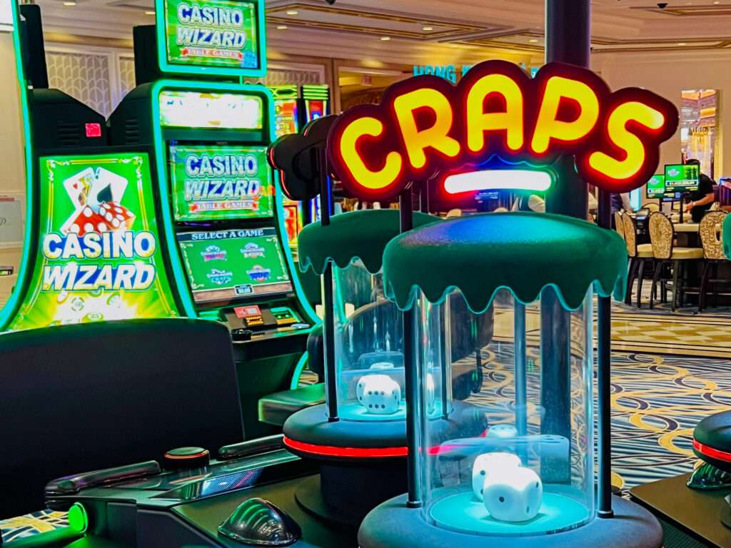 Photo of a casino gaming table. There are two green machines to the left - Casino Wizards. To the right are glass tubes with white dice inside. They have a yellow sign on top saying CRAPS.