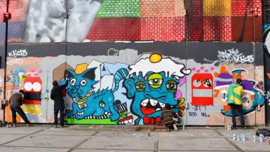 A number of graffiti artists at work spray painting a wall with blue cartoon characters
