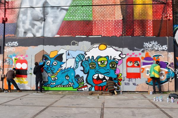 A number of graffiti artists at work spray painting a wall with blue cartoon characters