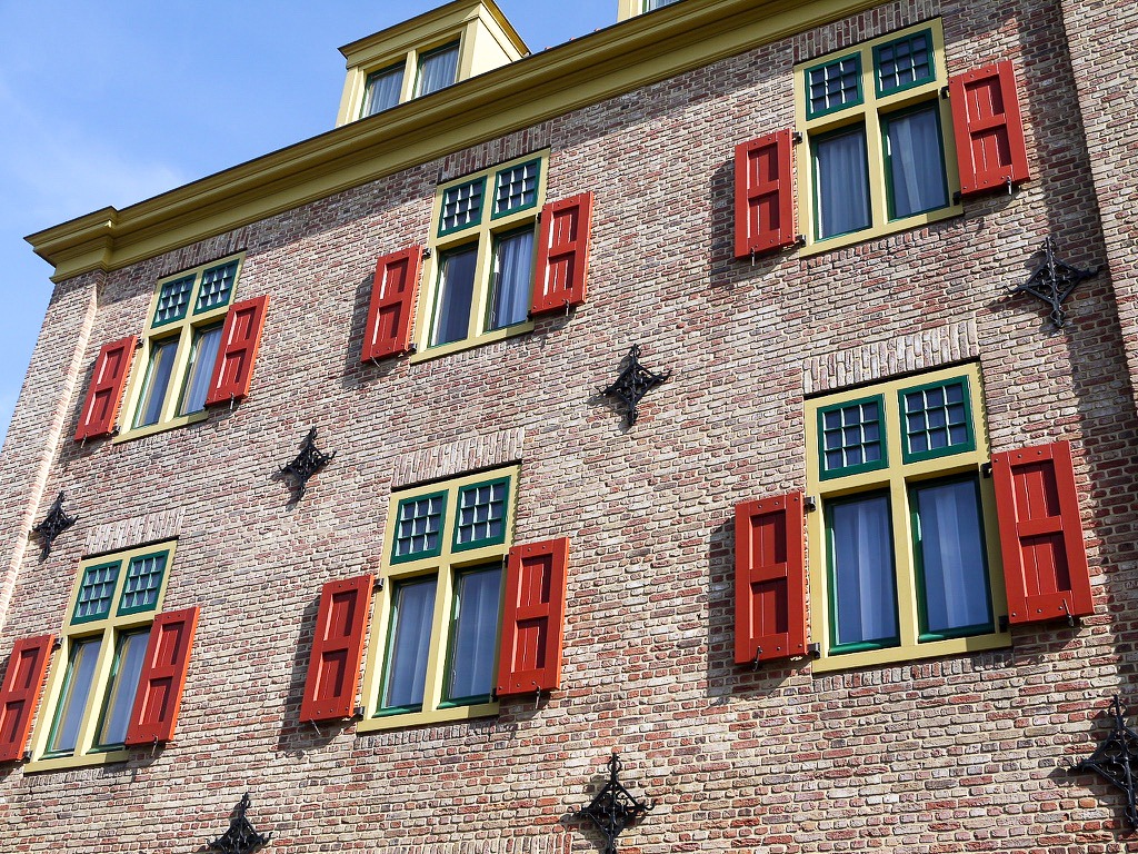 Looking up at a pale red brick building with two rows of rectangular windows with cream frames and red shutters. Blue sky above