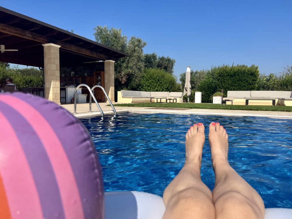 View from a sun lounger on a swimming pool. Plastic ball to the left, pair of legs to the right