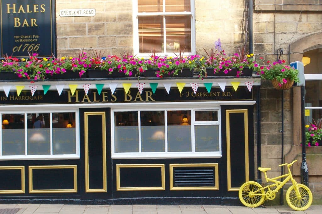 Photo of the front of a pub painted black with white woodwork. It has bunting and flowers over the windows and a yellow bike to the right hand side