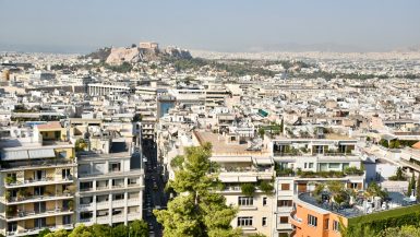 Cityscape view from a hillside looking across a city of white buildings and a hill in the distance with historical temple on top