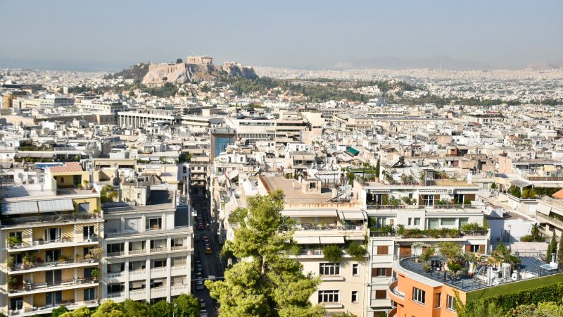 Cityscape view from a hillside looking across a city of white buildings and a hill in the distance with historical temple on top