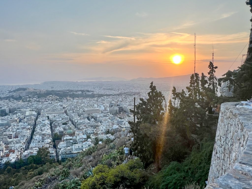 View of orange sunset from hilltop position overlooking a city of white buildings spread beneath you