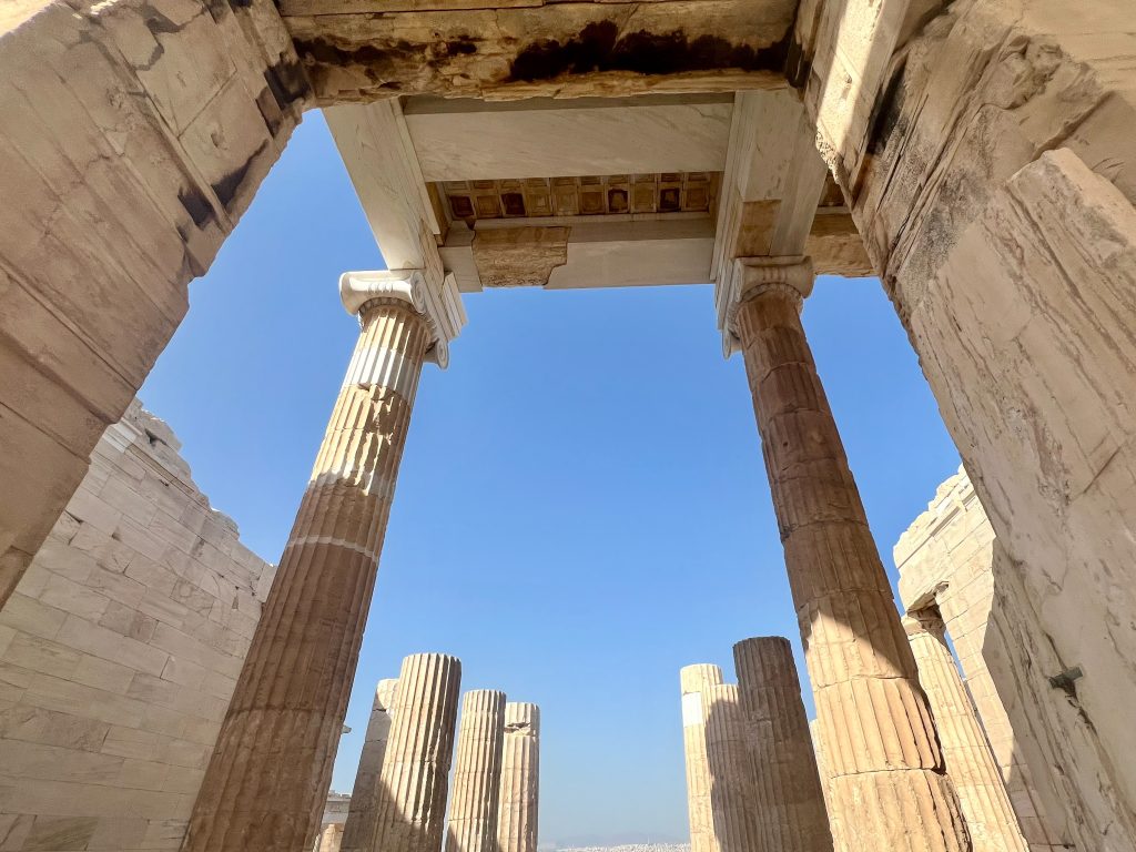 View upwards through an impressive gateway of pillars, with 8 pillars in the background against a blue sky