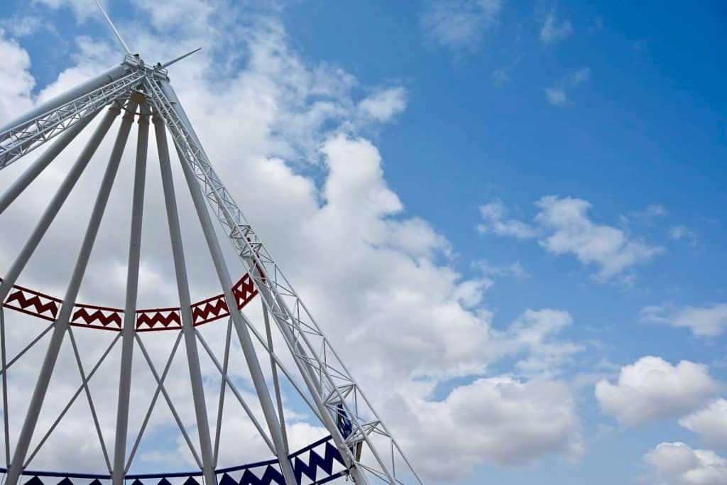 Blue sky with large white fluffy clouds. On the left is the structure of a large white teepee