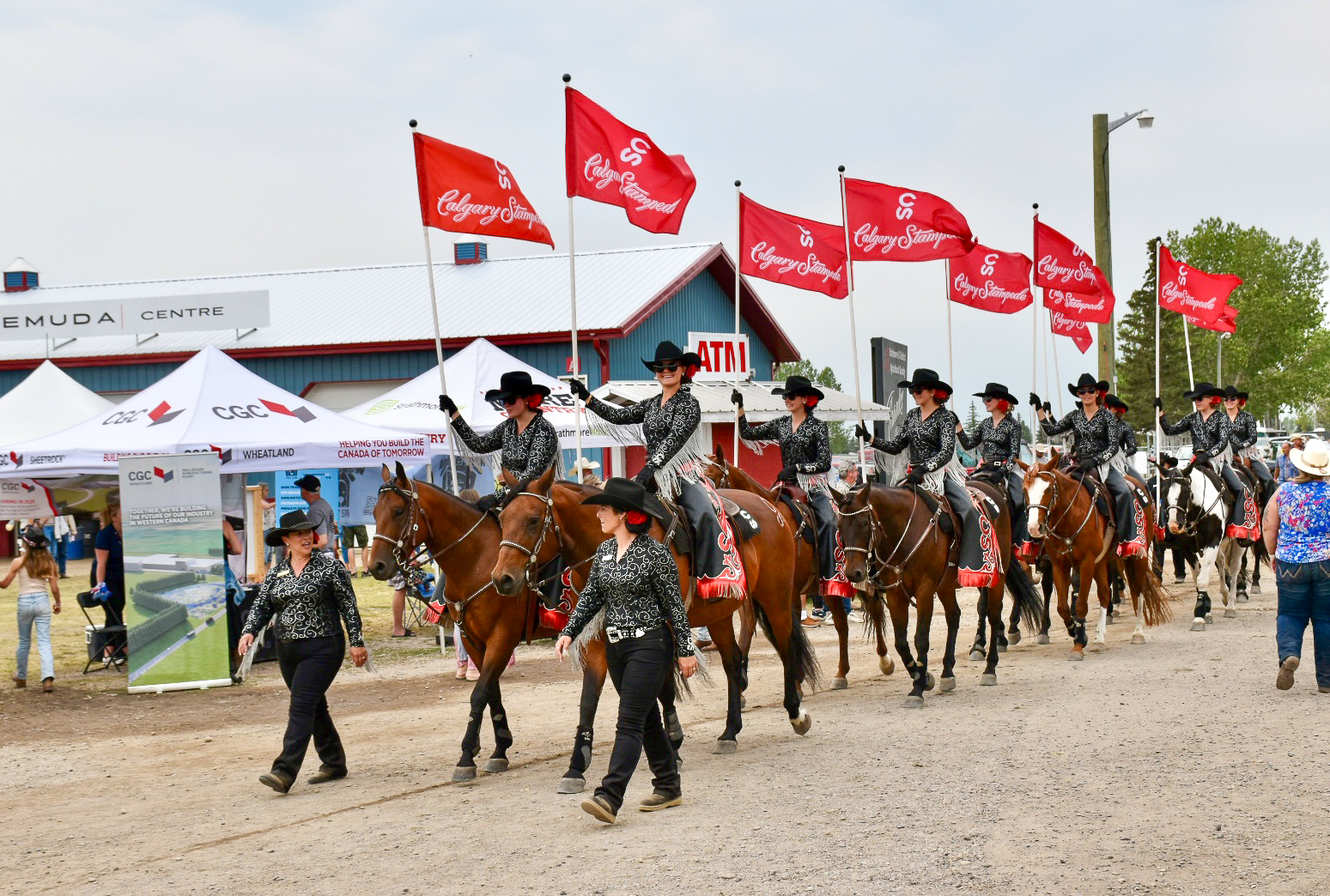 Double row of lady horseback riders in cowboy hats entering an arena with red flags