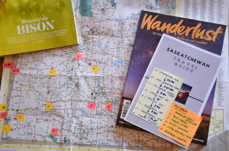 Map with travel books laid on top - Wanderlust Magazine and Saskatchewan travel guide. Post it notes on the map showing key positions