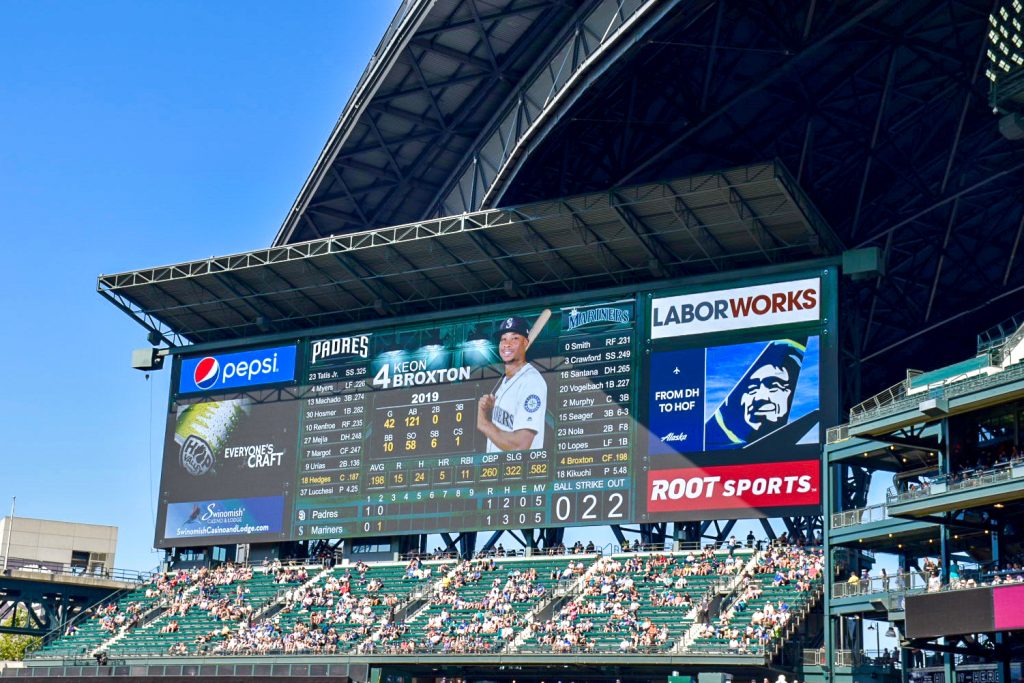 Image of a baseball scoreboard behind a section of audience seating. Scoreboard features Padres baseball player