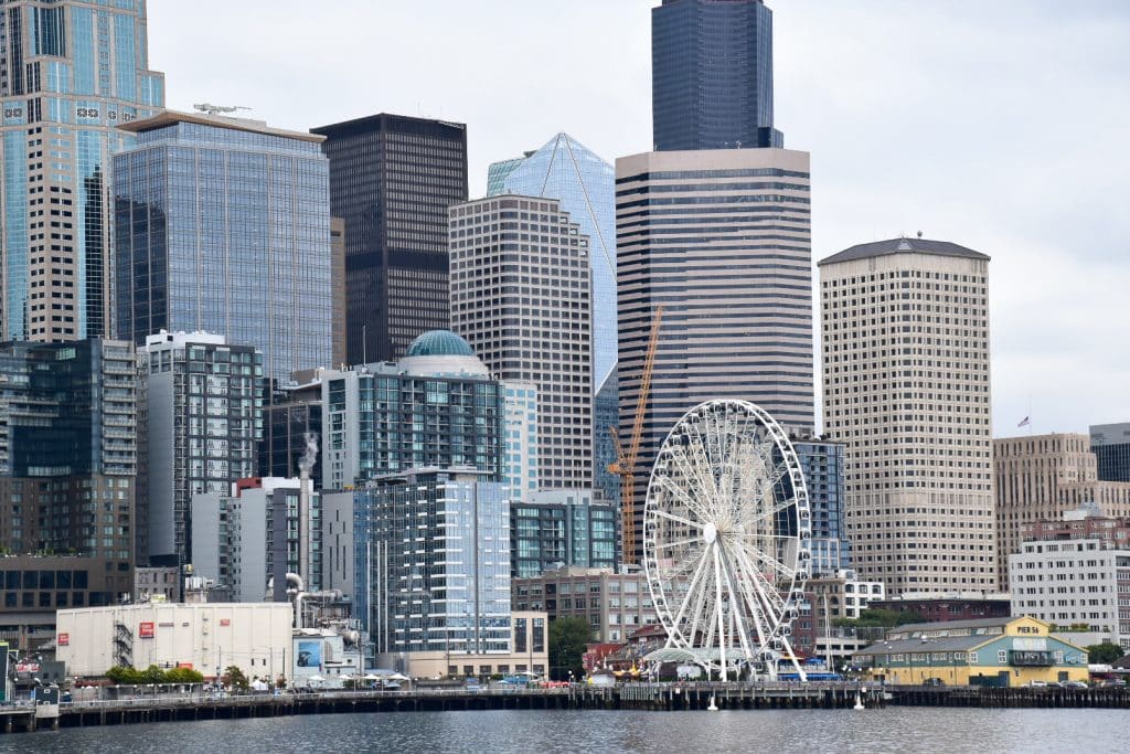 City scape taken from the water. You can see a variety of office blocks and sky scrapers, with a white sightseeing wheel in foreground