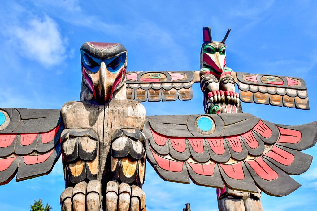 Pair of totem poles carved out of wood and painted. Image taken upwards towards the blue sky.