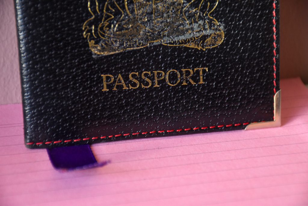 Black leather passport cover with red stitching and purple ribbon showing at the bottom, sitting on pink lined cards