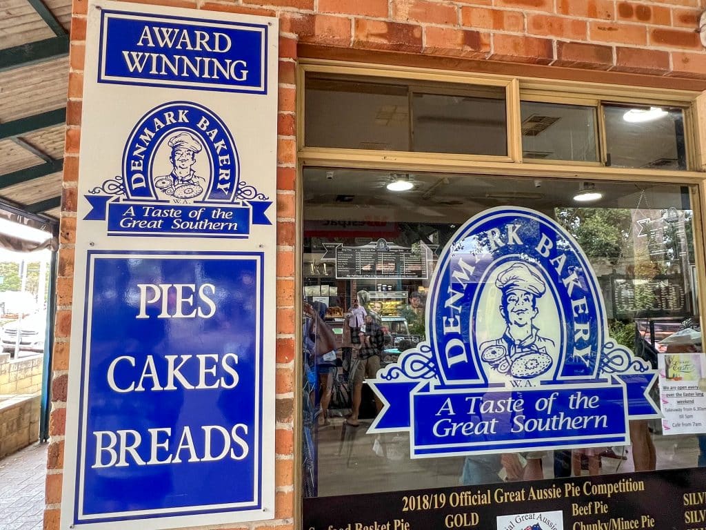 Photo of a shop window with blue and white signage for the Denmark Bakery advertising award winning pies, cakes, breads. A taste of the Great Southern. Window into the pie shop gives a hint of what's inside