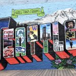 A multicoloured wall mural features 'Greetings from SEATTLE'. there is a mountain behind the word Seattle