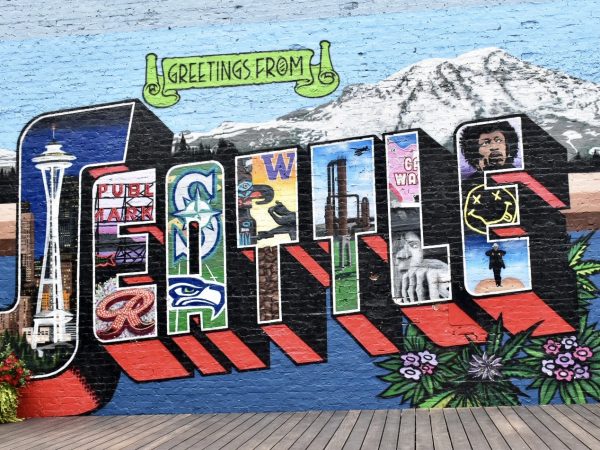 A multicoloured wall mural features 'Greetings from SEATTLE'. there is a mountain behind the word Seattle