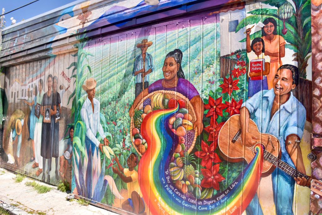 Colourful mural on garage doors featuring Latino peoples picking fruit and playing guitar