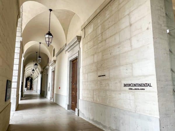 View down an external corridor of white stone with arches and black hanging lanterns all the way down. On the right hand side is a sign saying InterContinental in black letters on white stone brick wall
