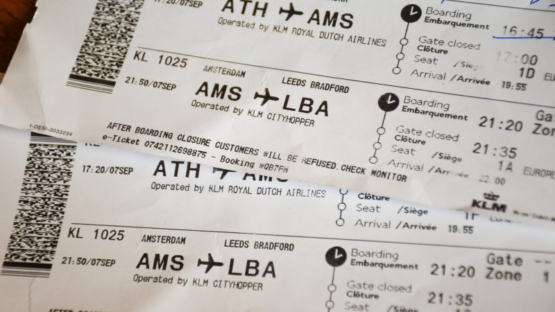 Frame is filled with close ups of two white airline boarding cards - one along the bottom and one at an angle across the top right. Printed writing shows that they are for a flight from Amsterdam to Leeds Bradford on KLM CityHopper