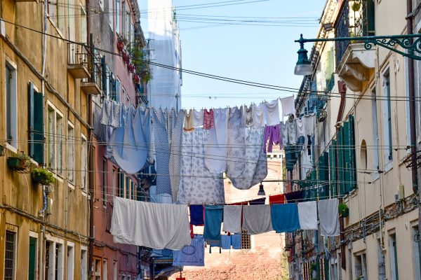 Lines of washing strung between two tall buildings with shutters and iron balconies. Sheets, towels and clothes hang in-between