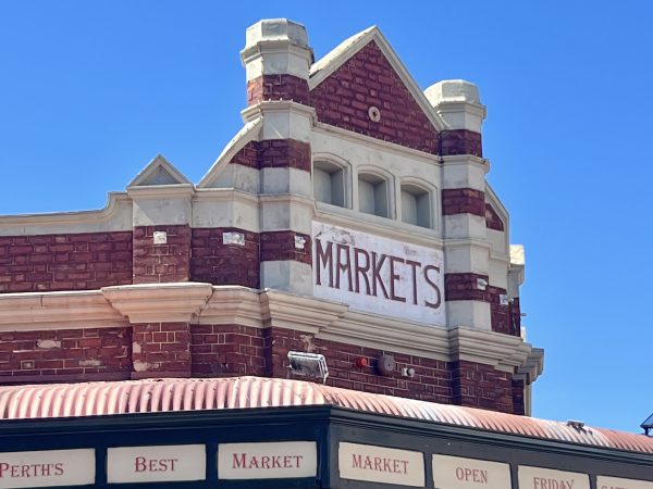 The roof of a red brick building against a clear blue sky. The building has a sign saying 'Markets' on the front, and then signs saying 'Perth's Best Market' around the bottom