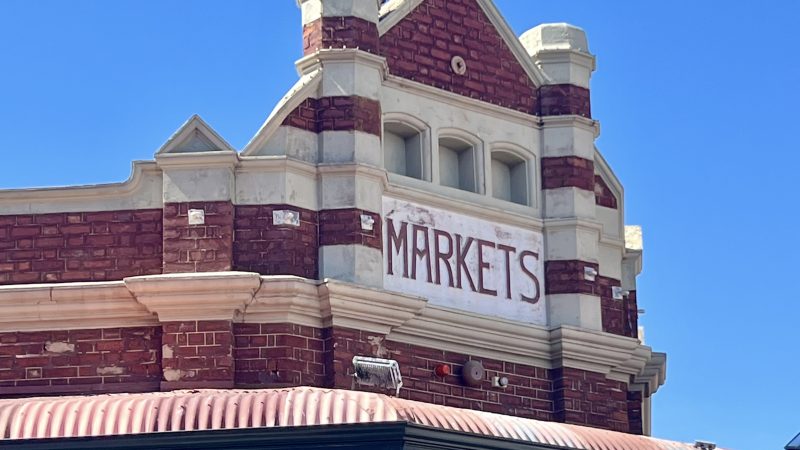 The roof of a red brick building against a clear blue sky. The building has a sign saying 'Markets' on the front, and then signs saying 'Perth's Best Market' around the bottom