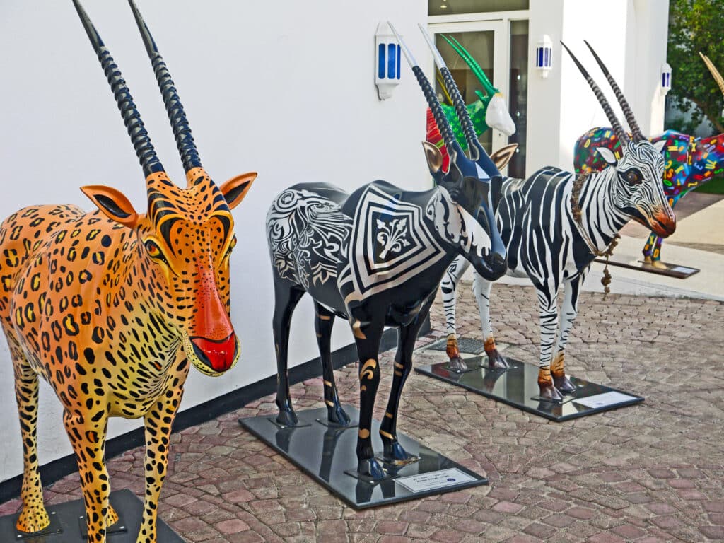 Row of multi-coloured painted antelope sculptures outside white building