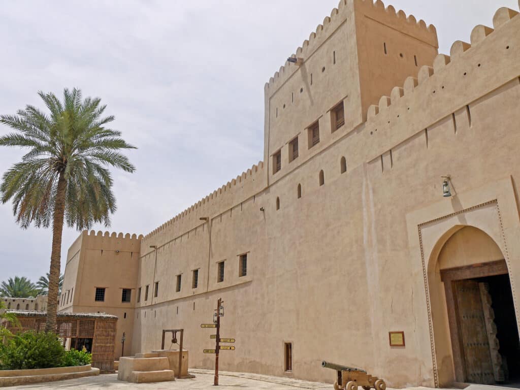 Sand coloured Arabic fort with palm tree to the right