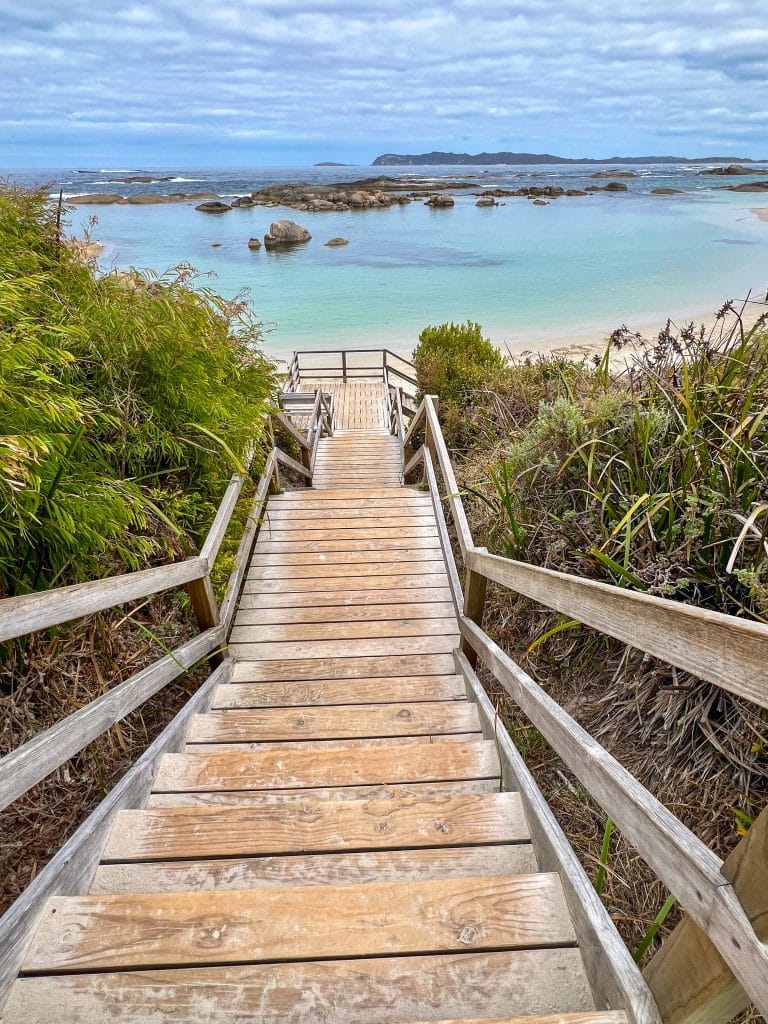 Wooden stairway leading down to clear turquoise water in the top half of the photo. Cloudy blue sky at the top