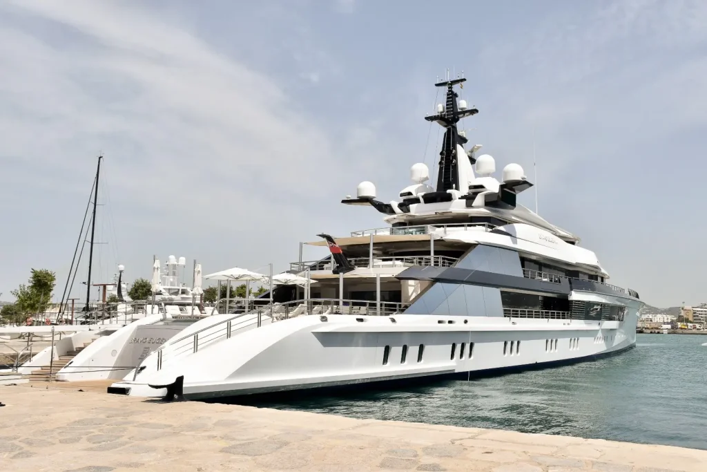 Large white luxury yacht moored by side of marina. Grey sky above