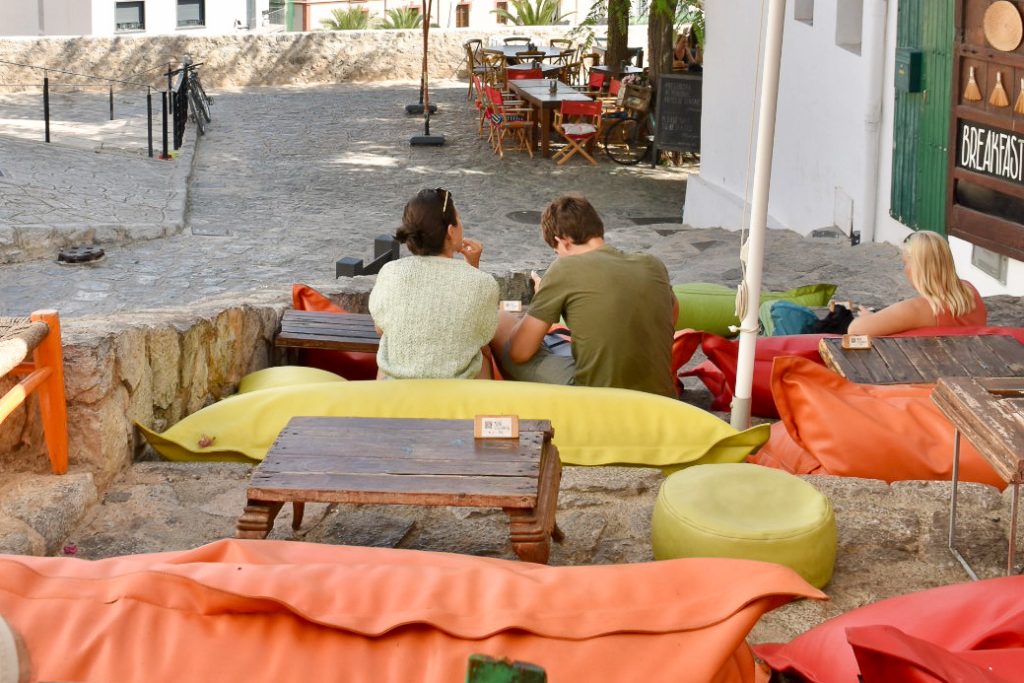 Looking down wide steps with rows of beanbags set out along with low wooden tables - beanbags are orange, red and lime green. A cafe is visible at the bottom of the steps. A couple sit on the bottom step and a lady to the right