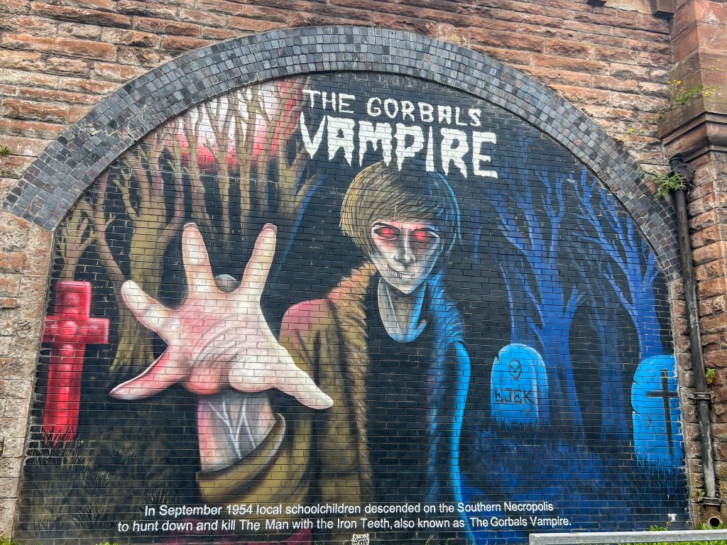 Mural painted within an arch in a brick wall (possibly a bridge). The mural is of The Gorbals Vampire and features a graveyard scene with a vampire in the middle reaching towards the camera