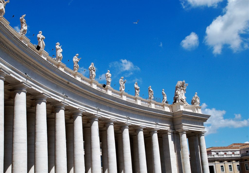 Colonnade with row of statues along the top. Blue sky behind.