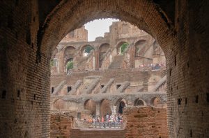 Looking through a brick archway towards the tiered sides of what looks like an amphitheatre. You can see groups of people making their way around the site