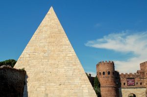 White stone pyramid to the left of the frame. Blue sky behind. Castle like building bottom right
