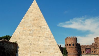 White stone pyramid to the left of the frame. Blue sky behind. Castle like building bottom right