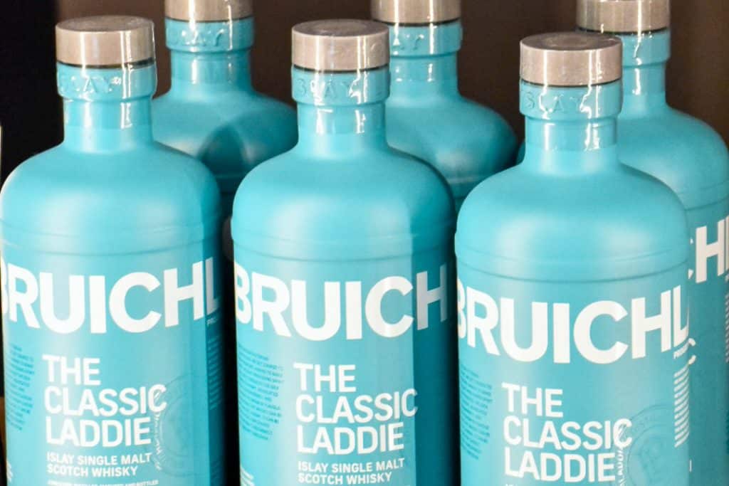 Row of 3 turquoise bottles across the middle of the frame, and a second row of 3 bottles behind. Each bottle has white writing - Islay Single Malt Scotch Whisky, The Classic Laddie, Bruichladdich