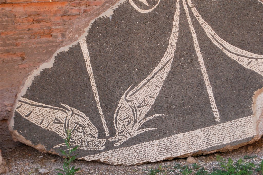 Slab of stone featuring tiny mosaic pieces leaning against a wall. You can see the design of 2 fish in white squares on a black background