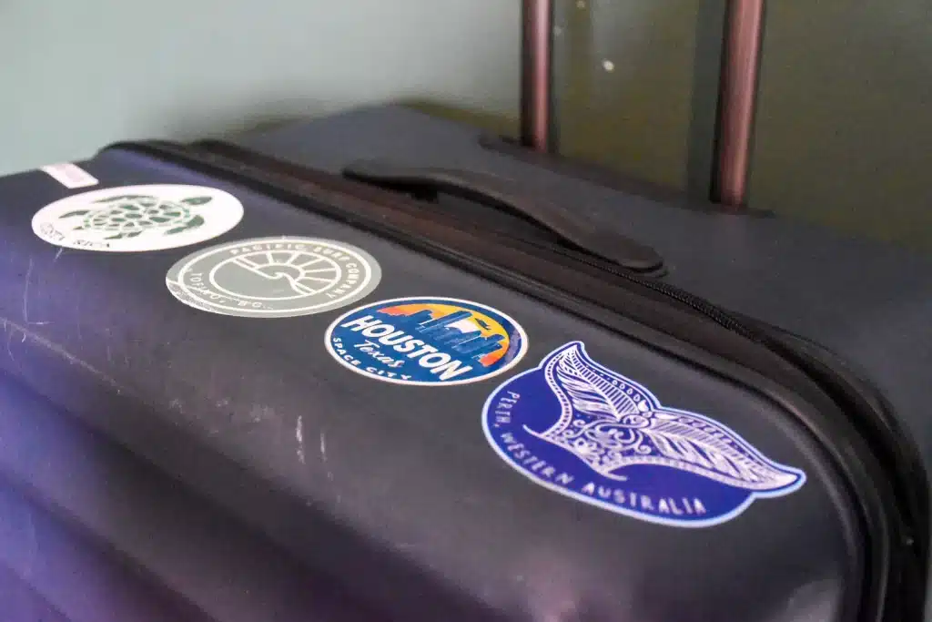 Top of a navy blue suitcase featuring a row of stickers. From the left - Costa Rica turtle, Great Tofino circle, Houston circle, blue whale tale for Perth